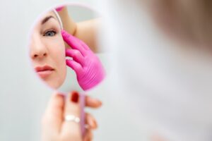 Woman looking at her face in a mirror considering a facelift or fillers in Los Altos, CA